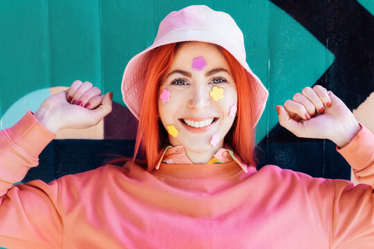 Emotional smiling woman with peach color hair and sweatshirt, bucket hat and flower stickers on her face. Anime style. Summer spring urban fashion. Vanilla Girl. Kawaii vibes. Candy colors design.