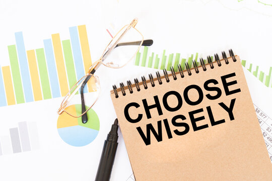 Notebook with CHOOSE WISELY text and eyeglasses on statistical charts. Business decision-making and analysis concept