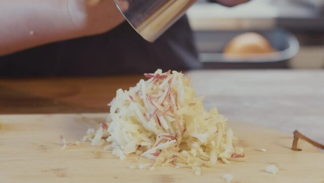 Close up of a woman hands, female chef grating an apple on a metal grater, on a wooden board in the kitchen. Interior, studio lighting. . High quality 4k footage