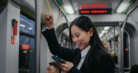 Pretty woman chatting with someone on phone and holding safety handle with other hand. Asian female...