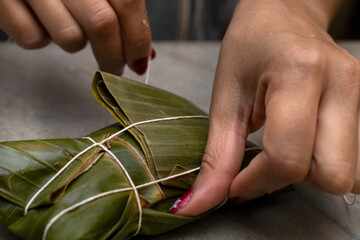 Woman's hands tying a hallaca or tamale in a banana leaf. Traditional food