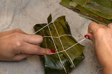 Woman's hands tying a hallaca or tamale in a banana leaf. Traditional food