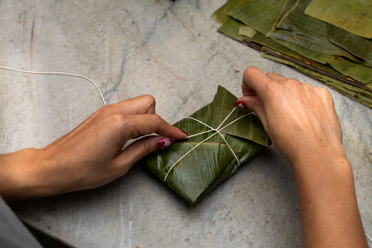 Woman's hands tying a hallaca or tamale in a banana leaf. Traditional food