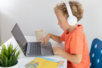 Little boy with headphones and blonde hair plays with a laptop