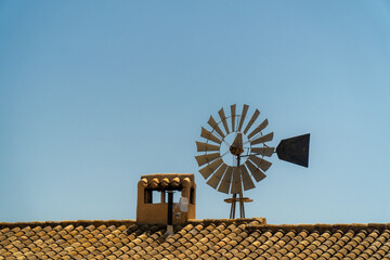 Old windmill on the roof of a country house, blue sky, sunny summer morning