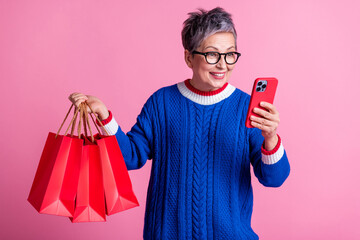 Photo of nice aged lady use phone hold mall bags wear blue sweater isolated on pink color background