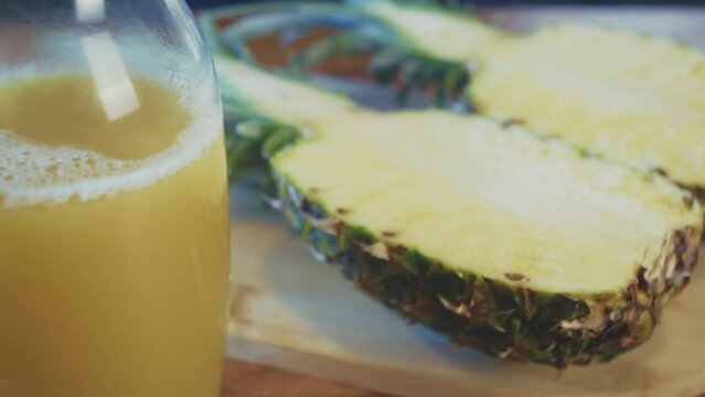 Bottle of freshly pressed pineapple juice with a pineapple sliced in half in the background in a brightly lit kitchen. Studio shot. High quality 4k footage