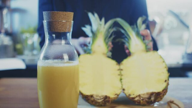 Close up of woman's hands opening a sliced pineapple with bottle of fresh pineapple juice in front. Female cook, chef in a brightly lit kitchen. Studio shot. High quality 4k footage