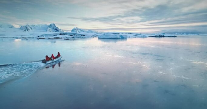 Antarctica travel and exploration, people riding motor boat. Zodiac boat sailing cold polar ocean water surface in sunset light. Discover the beauty of South Pole. Aerial winter landscape, drone pov