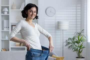 Smiling woman showcasing weight loss by holding large jeans