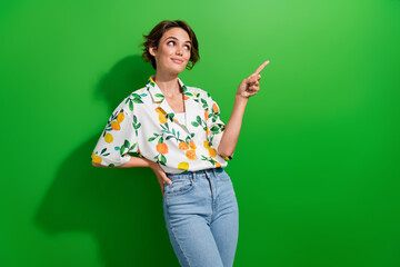 Photo of good mood dreamy lady wear print shirt looking showing finger empty space isolated green...