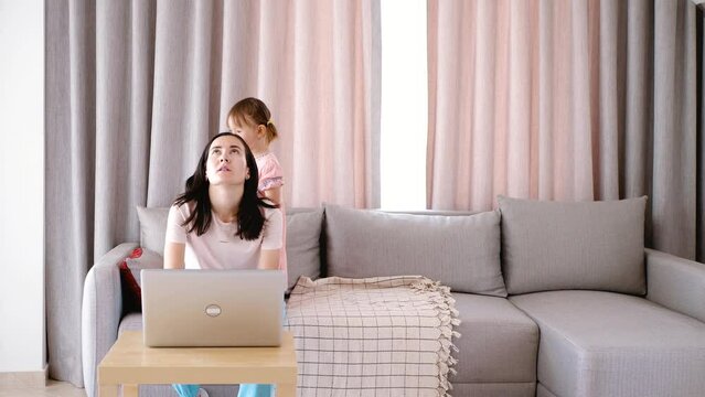Mom tries to work from home online, but the child jumps on the sofa and prevents her from concentrating