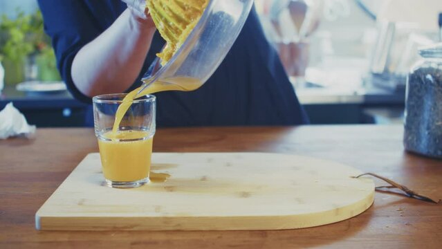 Close up of woman's hands pouring freshly pressed orange juice from manual juicer into a glass. Female cook, chef preparing orange juice in a brightly lit kitchen. Studio shot. High quality 4k footage