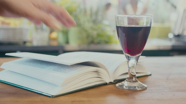 Close up of woman's hands taking eyeglasses and a glass of wine and a book in a brightly lit kitchen. Preparing for relaxation time. Lifestyle concept. . High quality 4k footage