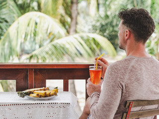 Handsome man having breakfast in an outdoor hotel restaurant. Male traveler drinking fresh juice in a modern cafe. Summer vacation. Concept of relaxation, travel and healthy eating