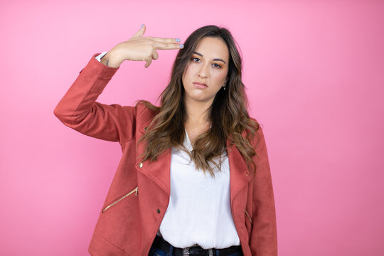 Young beautiful woman wearing casual jacket over isolated pink background Shooting and killing oneself pointing hand and fingers to head like gun, suicide gesture.