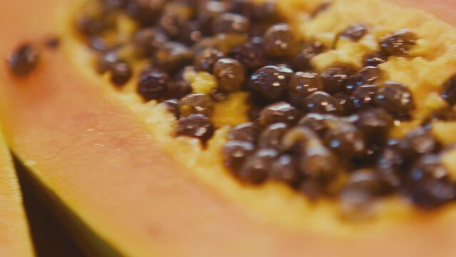 Close up of papaya fruit seeds, pawpaw fruit sliced in half using a knife. Preparing papaya in a brightly lit kitchen. Studio shot. High quality 4k footage