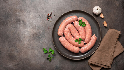 Raw sausages in a plate on a dark grunge background. Top view, flat lay, banner. - obrazy, fototapety, plakaty