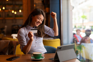 Happy woman holding credit card in coffee shop. Successful buying online