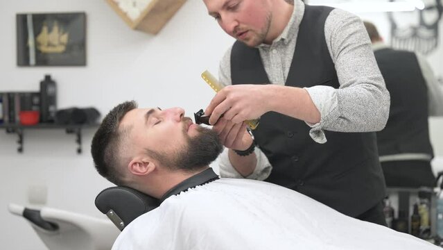A barber trims a Caucasian clients mustache with a trimmer.