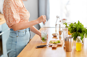 culinary, drinks and people concept - close up of woman with glass and spoon making lime mojito...