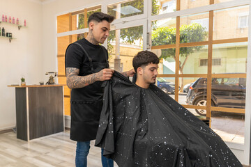 peluquero,barbero tatuado  cortando el pelo , la barba y el bigote a un cliente joven y moreno