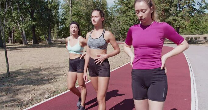 Three fit women in sportswear taking a break and a walk red sports track during their workout in a vibrant urban park.
