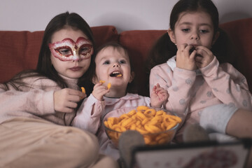 Three girls are watching a movie sitting on the couch.