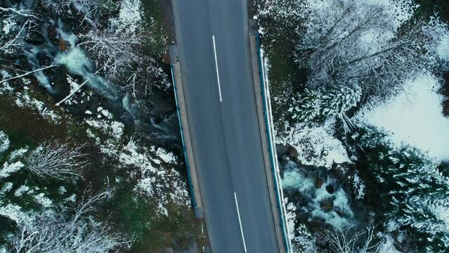 Top down aerial drone view on small car cross bridge of mountain river in forest. Cinematic winter location. Driving in mountains and forest