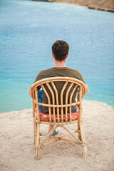 Happy guy sitting on a stool by the sea background on the nature - obrazy, fototapety, plakaty
