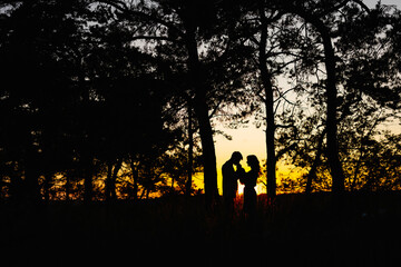 Silhouette of two people standing in front of trees - obrazy, fototapety, plakaty
