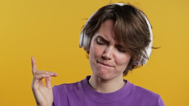 Positive smiling woman listening music, enjoying headphones, yellow background