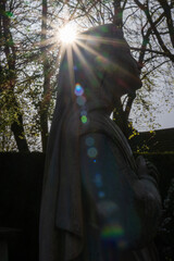Sun glare behind statue of Mary (Madonna) praying to The Lord after the crucifixion of Jesus Christ in the gardens of The English Martyrs Roman Catholic Church, Whalley, Lancashire, England 