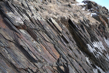 Closeup of dark gray rock with thin veins of red and brown, mountain wall, slanted close up,...