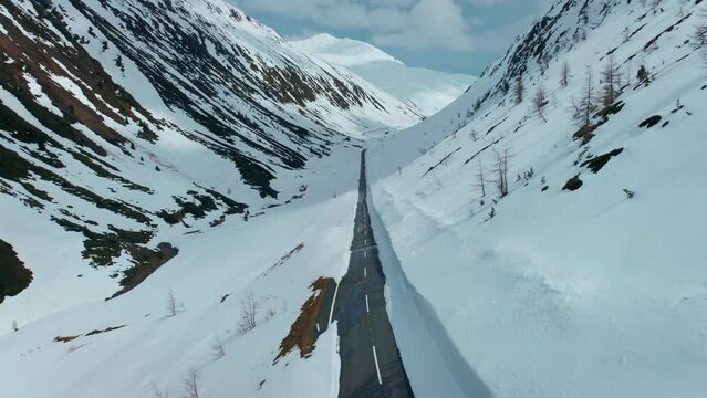 Aerial drone of empty mountain road with snow walls create corridor after heavy snowfall in winter season. Beautiful and cinematic mountain valley in the Alps, mountain pass cleared and open in spring