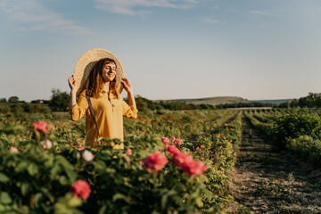 A woman wearing a straw hat stands in a field of pink flowers. She is smiling and she is enjoying...