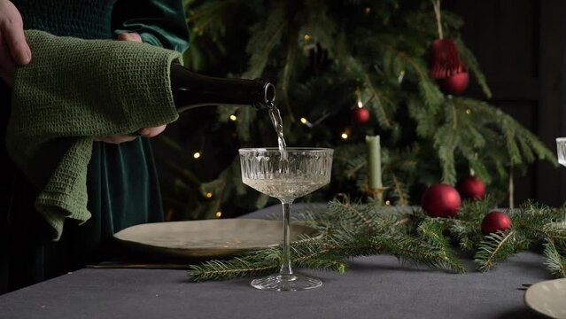 woman pours sparkling wine into glass goblet during christmas