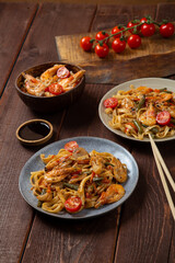 Rice with shrimp and udon in Pad Thai sauce on a wooden table next to cherry tomatoes, soy sauce and chopsticks