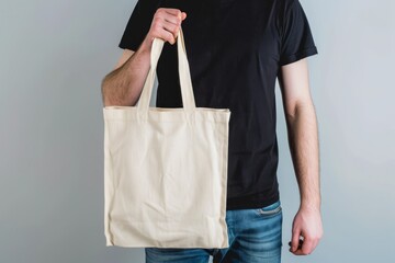   A man holds a white tote bag in his right hand and wears a black T-shirt