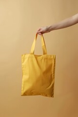   Person's hand holding a yellow shopping bag against beige backdrop Another hand lifting same-colored bag
