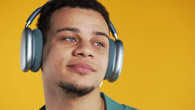 Positive mixed race man listening music, enjoying dance with modern headphones