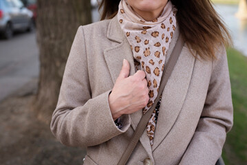 Beige coat and beige scarf with imitation leopard skin on woman outdoors, spring classic clothes for middle-aged women, close-up