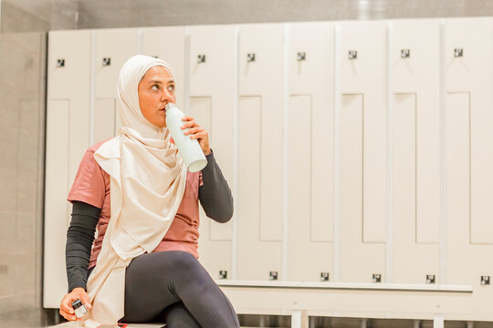 Muslim woman hydrating before yoga class in locker room