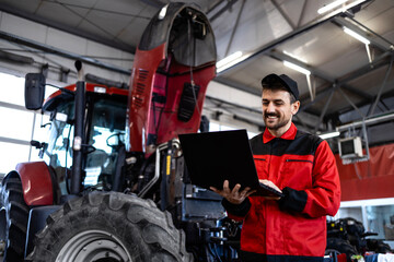 Professional serviceman standing by the tractor machine and holding laptop diagnostic tool.