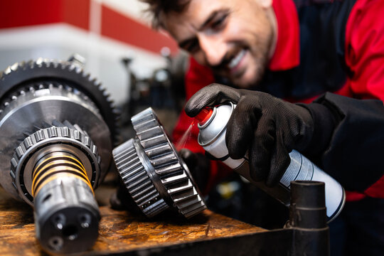 Smiling serviceman or mechanic repairing transmission gear box in workshop.