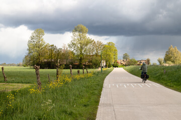 Lonely cyclist in the flowery rural landscape with dark threatening clouds. - obrazy, fototapety, plakaty