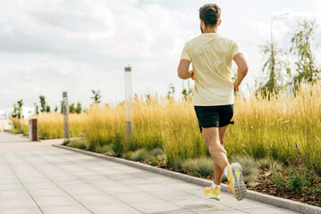 A man jogs in an urban park, the golden hue of tall grasses swaying in the background under a...