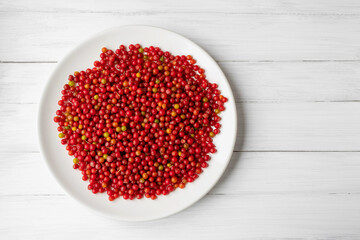 Red sea buckthorn berries, silver Shepherdia (lat. Shepherdia argentea) in a round plate on a white painted surface close-up, copy space. Alternative medicine