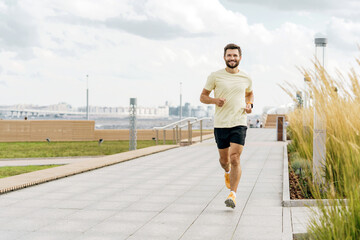 A cheerful man runs confidently on a promenade, with a cityscape and overcast sky as his backdrop.