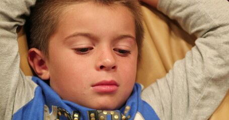 Candid little boy face seated on sofa paying attention to movie story